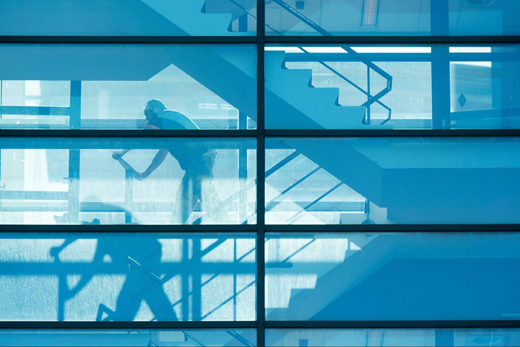 A modern architectural shot featuring a silhouetted figure through blue-tinted glass with stairs.